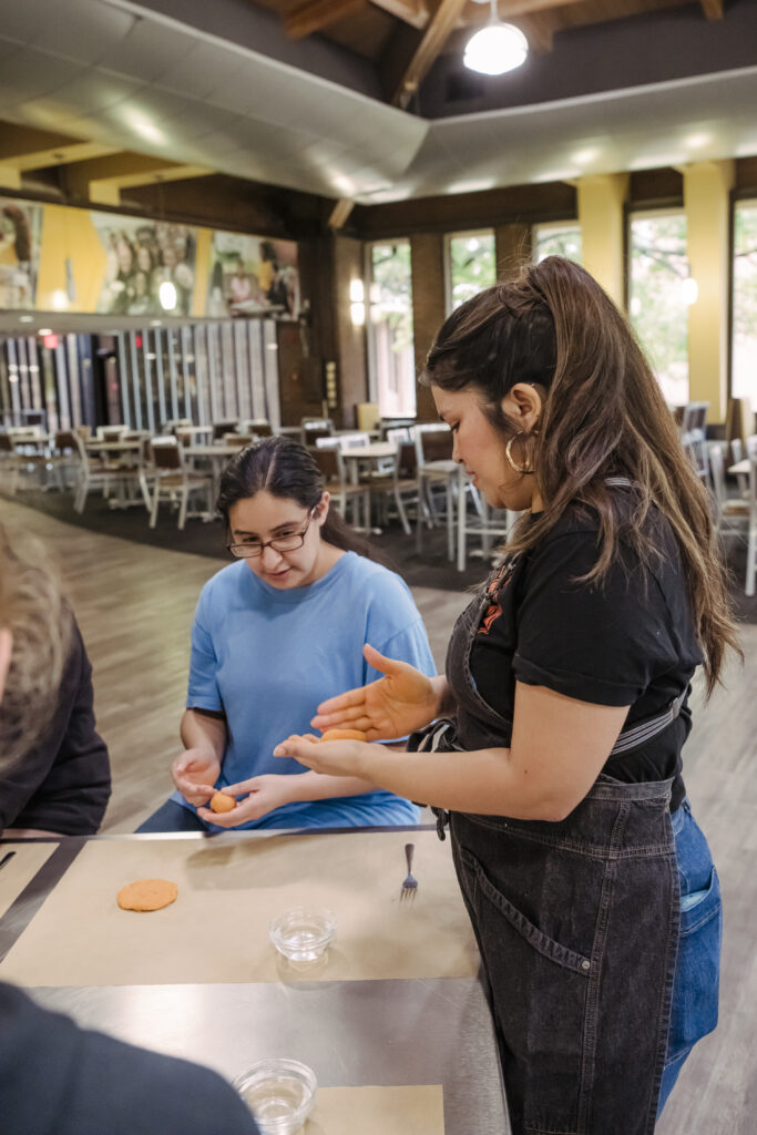 A UMBC college students sits at a cafeteria table watching a chef fold dough