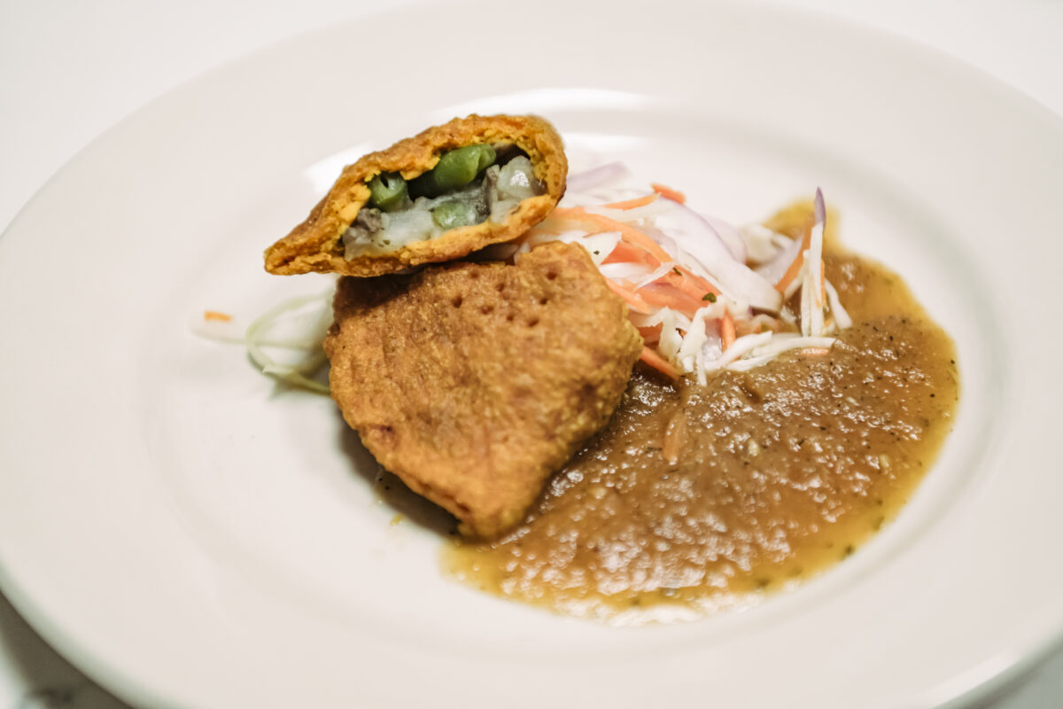 A white ceramic plate filled with a fried meat pie with slaw and salsa