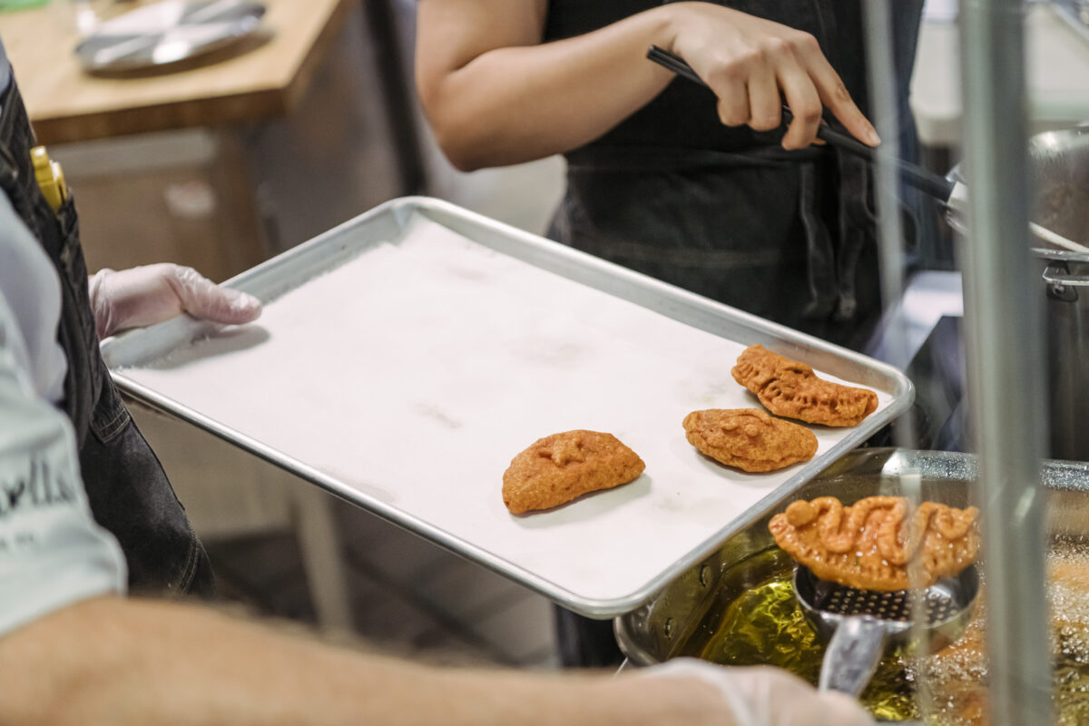 A chef scoops fried meet pies onto a stainless steel tray