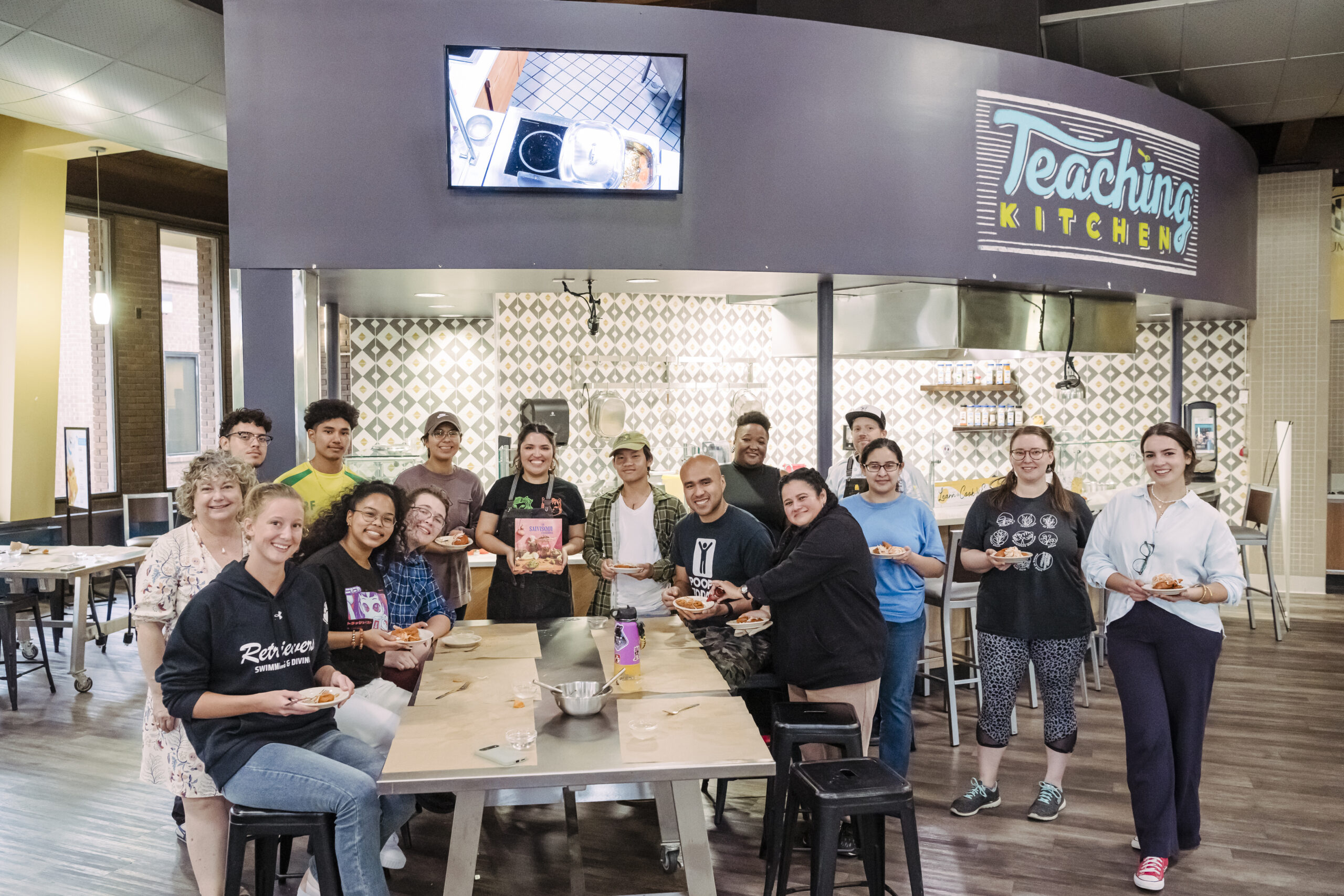 UMBC college students gather at True Grits' Test Kitchen holding small plates of Salvadoran pastelitos with chef Karla T. Vasquez