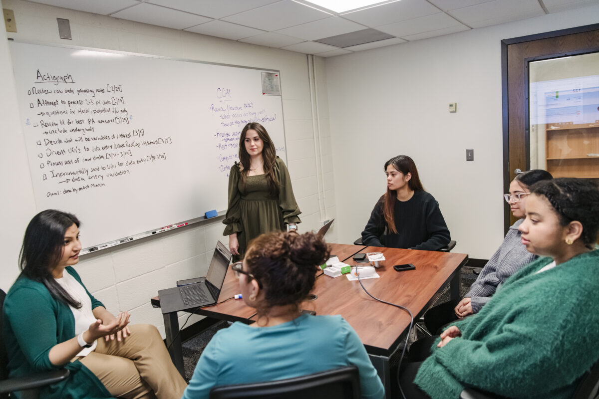 A professor sits with students to discuss research projects