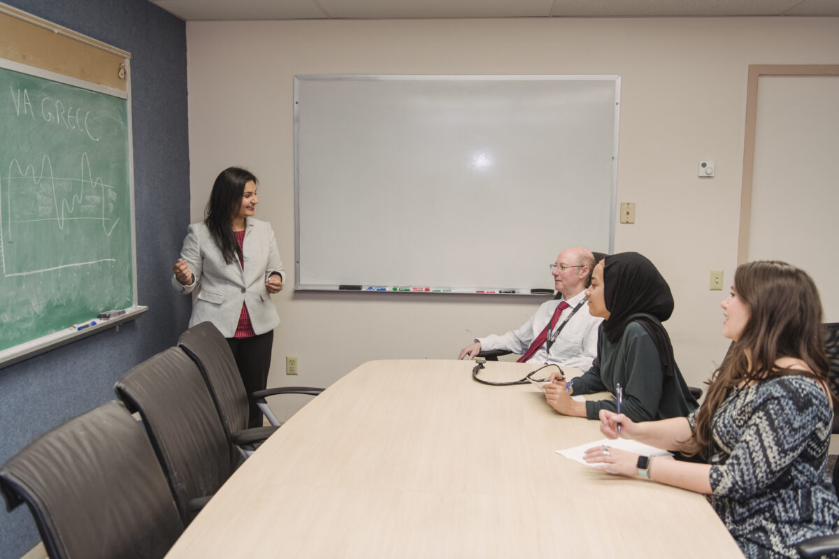 Tasneem Khambaty stands next to a chalk board discussing a graph about type 2 diabetes with three researchers sitting at a conference table