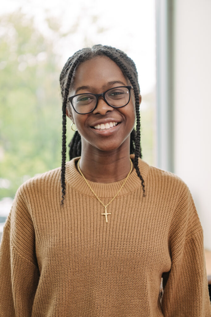 headshot of a woman with braids smiling with glasses and a cross necklace