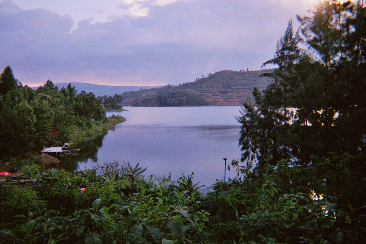 a large lake surrounded by lush greenery and red-orange terraced cliffs at sunset; the sky is a bluish purple with a slight orange glow at the horizon.