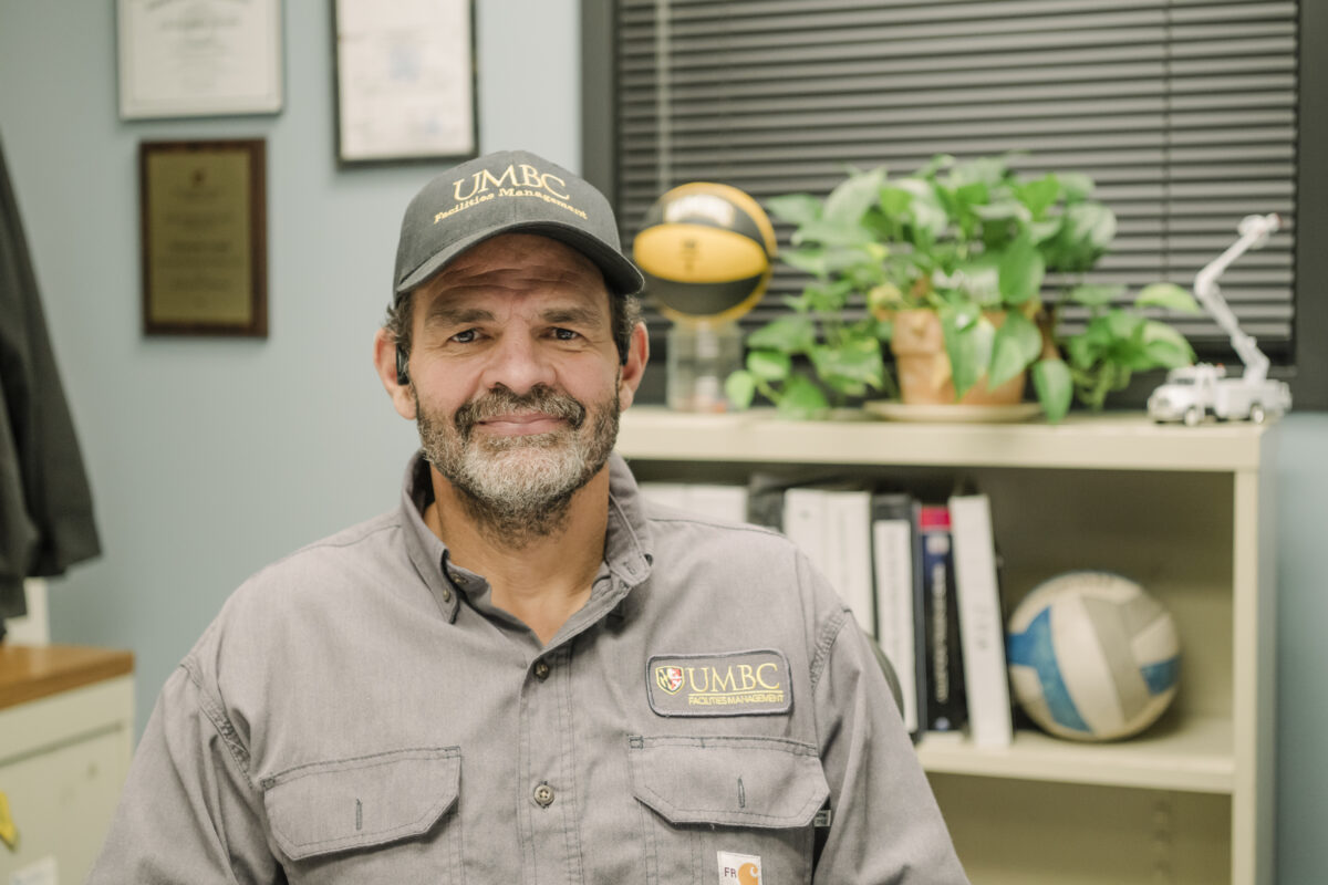 a man in a UMBC cap sits in his office