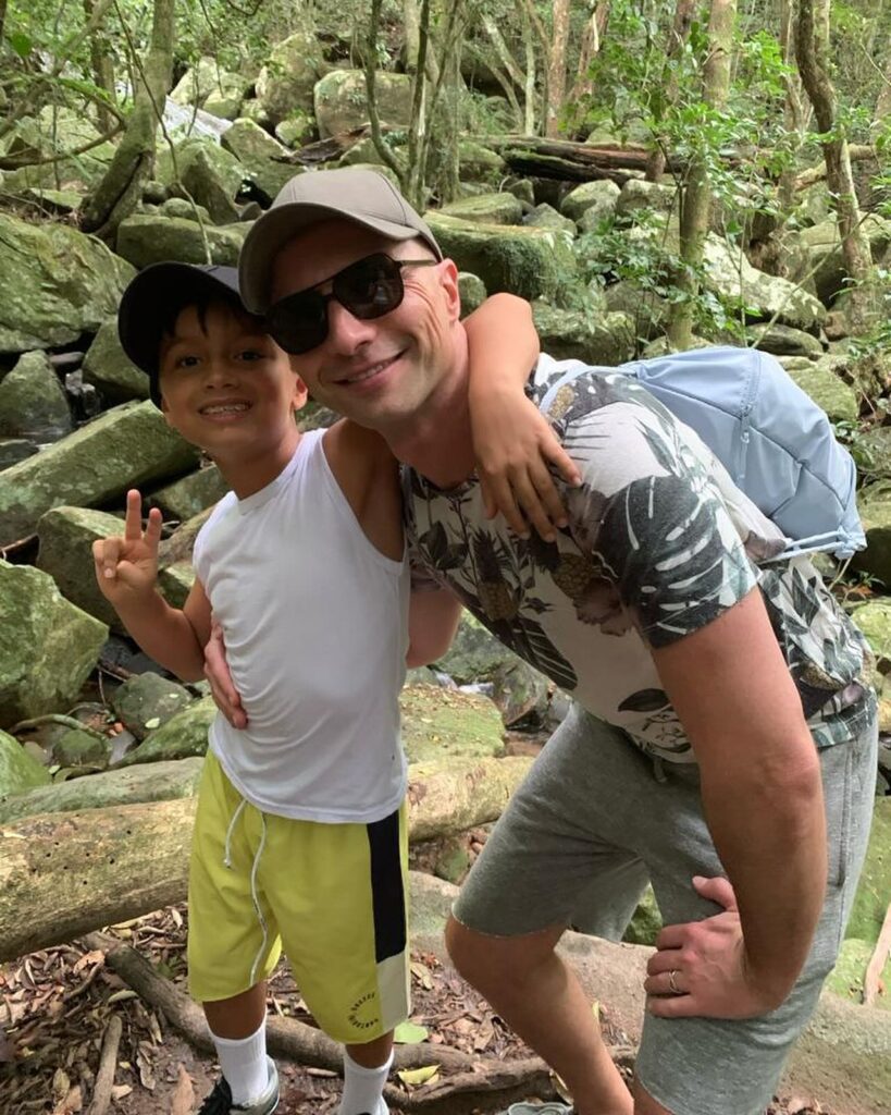 An adult and a child stand next to each other in a forest