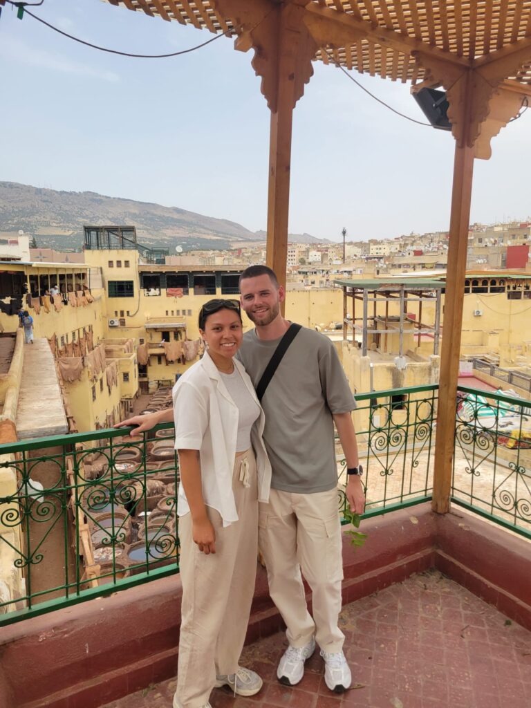 A couple in Rabat, Morocco stand on a balcony with a village behind them