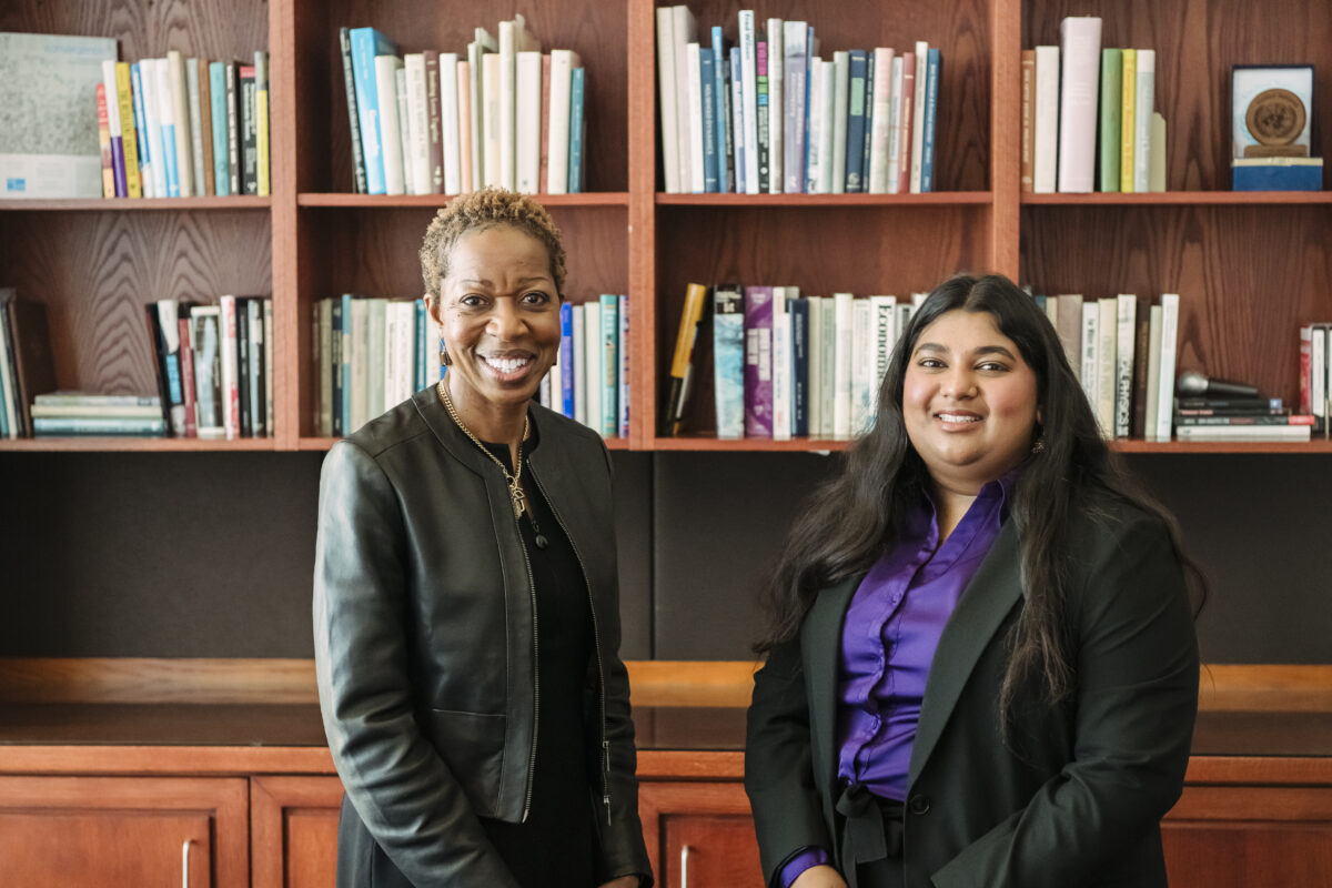 Meghna and UMBC President Dr. Valerie Sheares Ashby stand side by side in her office, both smiling warmly at the camera. Behind them is a wooden bookshelf filled with books, creating a professional yet inviting backdrop.