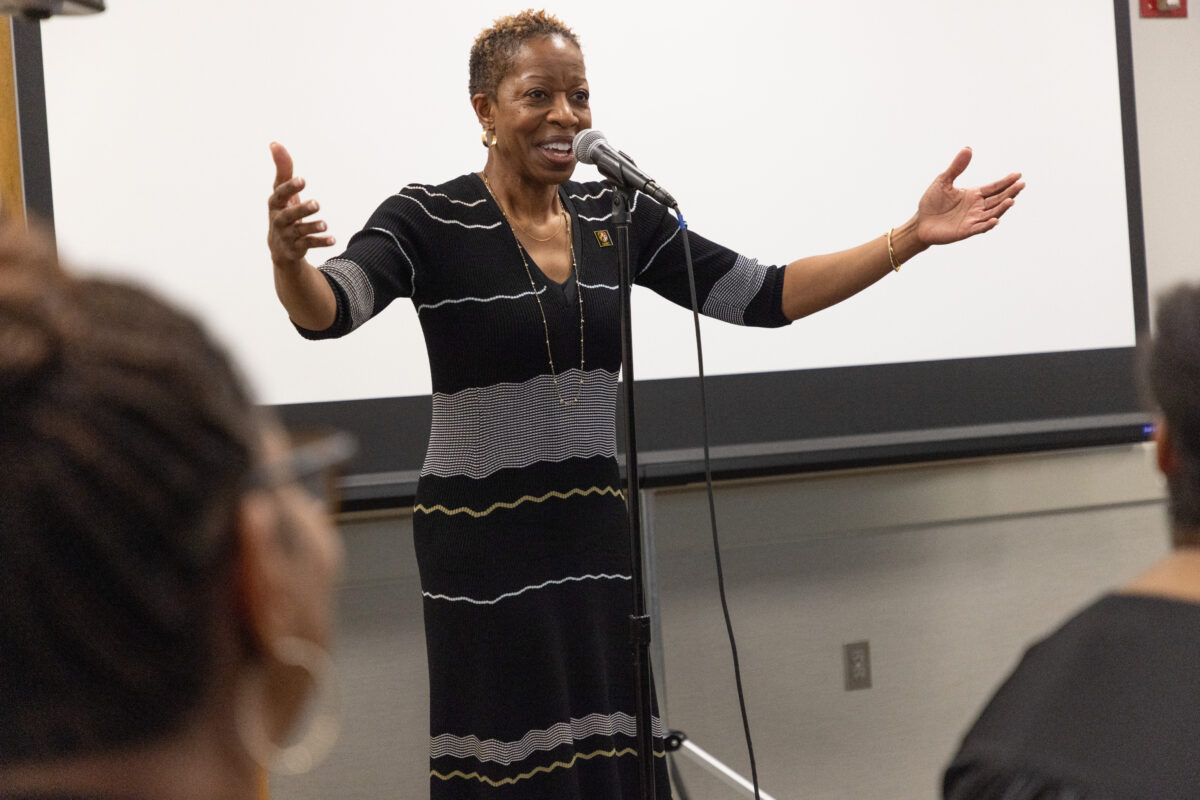 woman speaks at microphone with arms spread wide