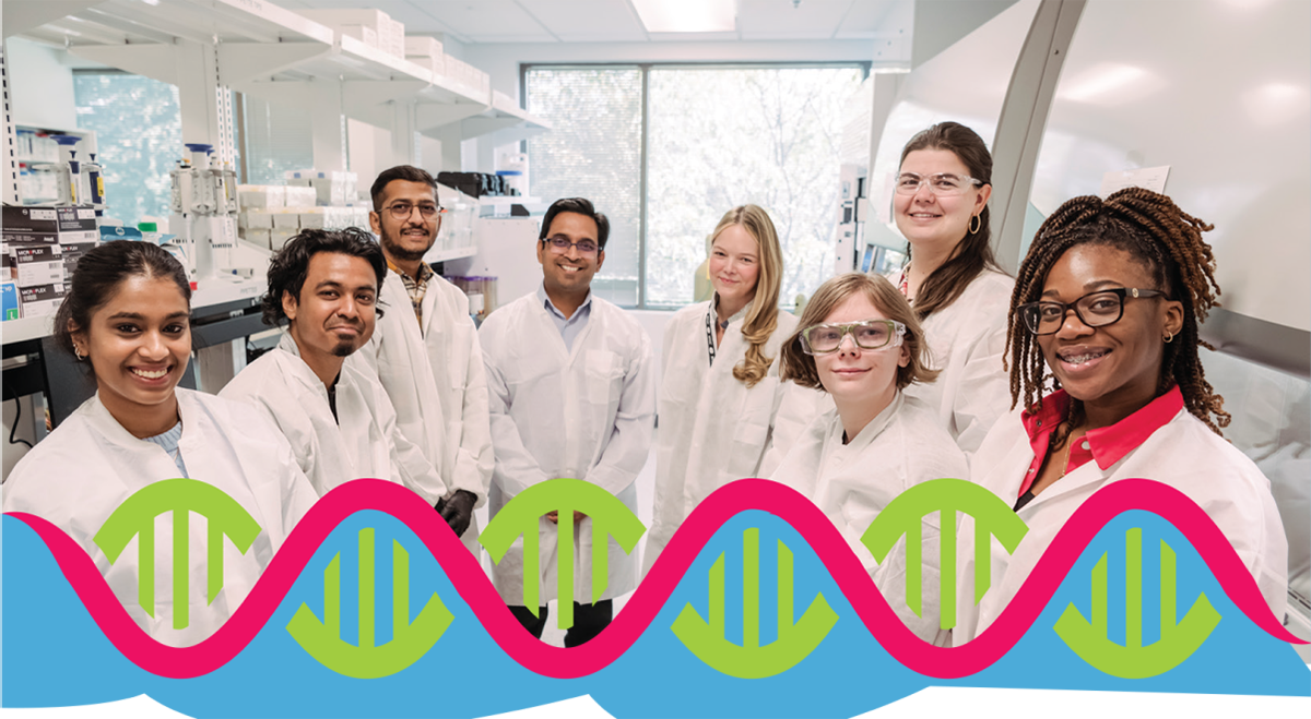 A diverse group of students wearing lab coats and standing in a lab together to pose for a photo