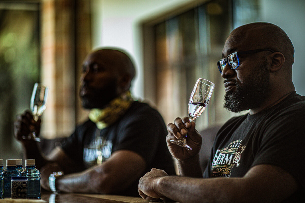 two men sit at a bar sipping clear liquid in glasses