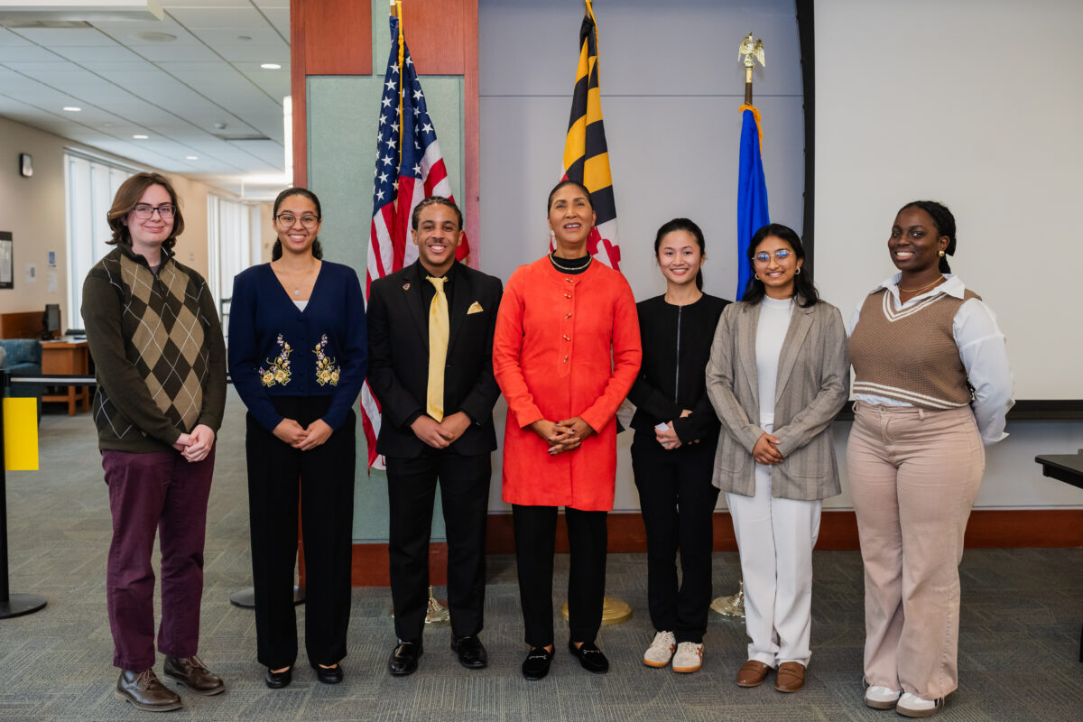 Six UMBC college students gather around Cheryl R. Campbell, the assistant secretary for administration for HHS at a press conference