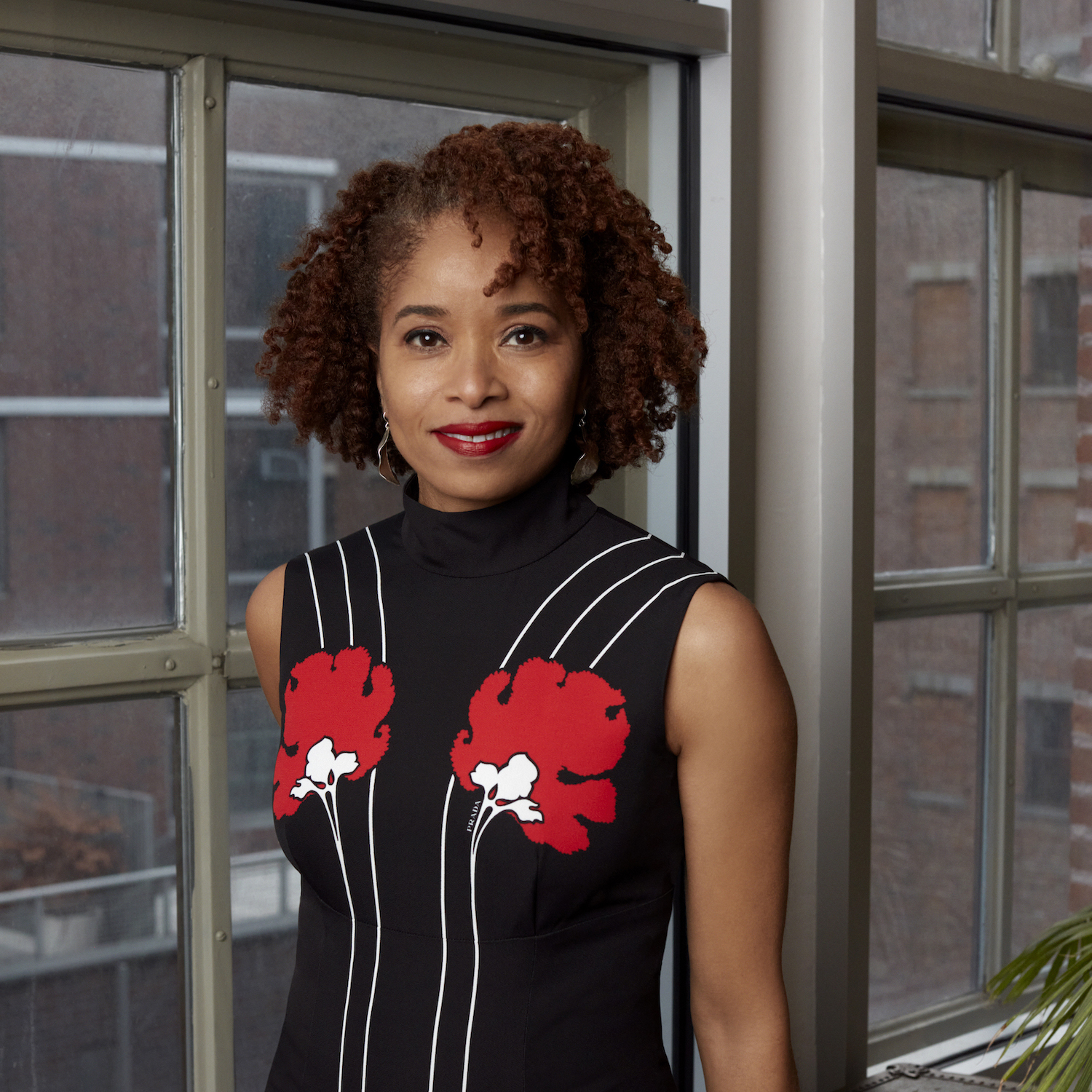 A portrait of Nicole R. Fleetwood, a Black woman, wearing a black dress with red flowers on it.