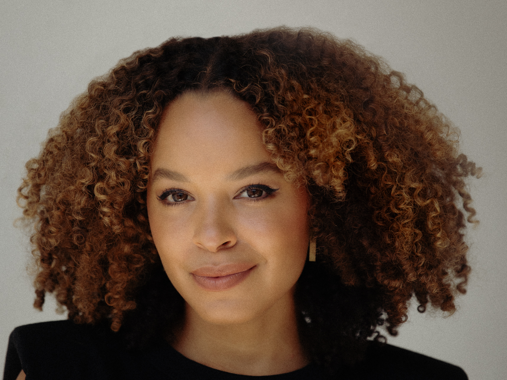 A portrait of Antonia Hylton, a Black woman with red curly hair. She is wearing a black-colored blouse.