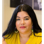 Ashley Minner Jones, an indigenous woman, wearing a golden yellow blouse. She has long dark hair.