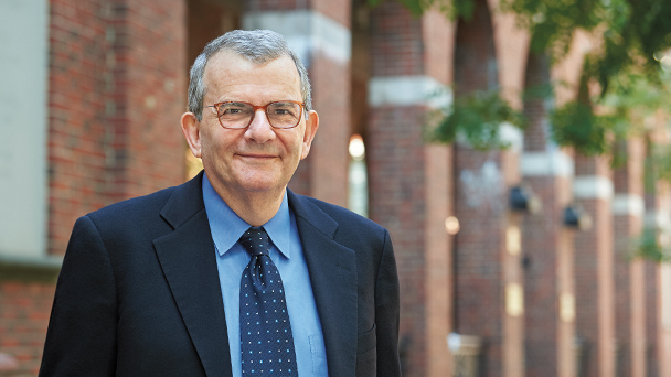 Samuel Scheffler is in a blue suit and tie standing in front of a brick building. He is wearing glasses.