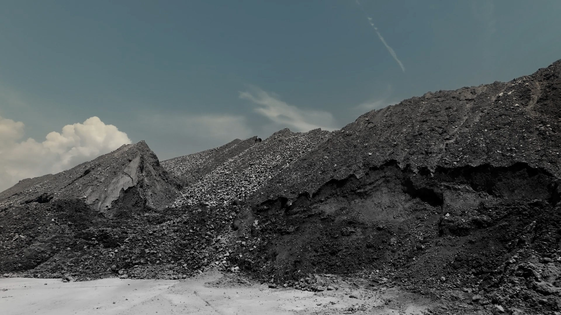 Mounds of black and gray sand and small rocks in front of a muted blue sky.