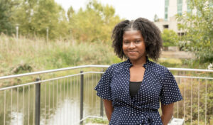 Emmanuella Osei, a college student wearing a black blouse stands near a rail overlooking a pond