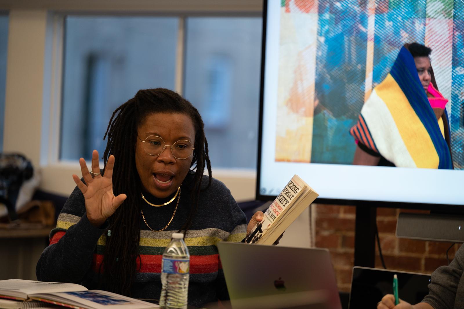 Tomashi Jackson, a Black woman, speaks while gesturing with her right hand. The image of another woman, Nia Evans, is seen on a screen to the right.