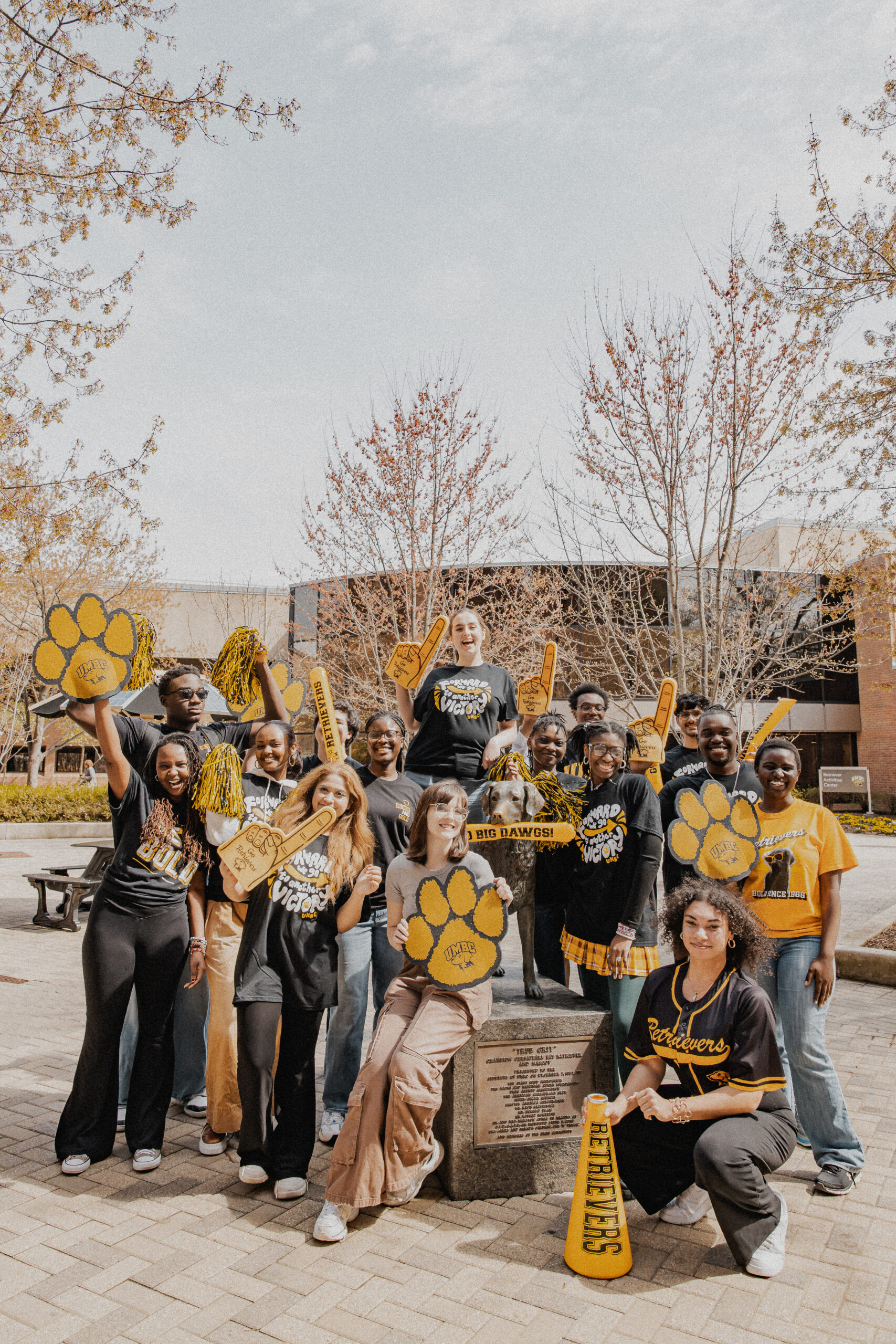 a diverse group of students in UMBC spirit-wear, standing around the mascot statue