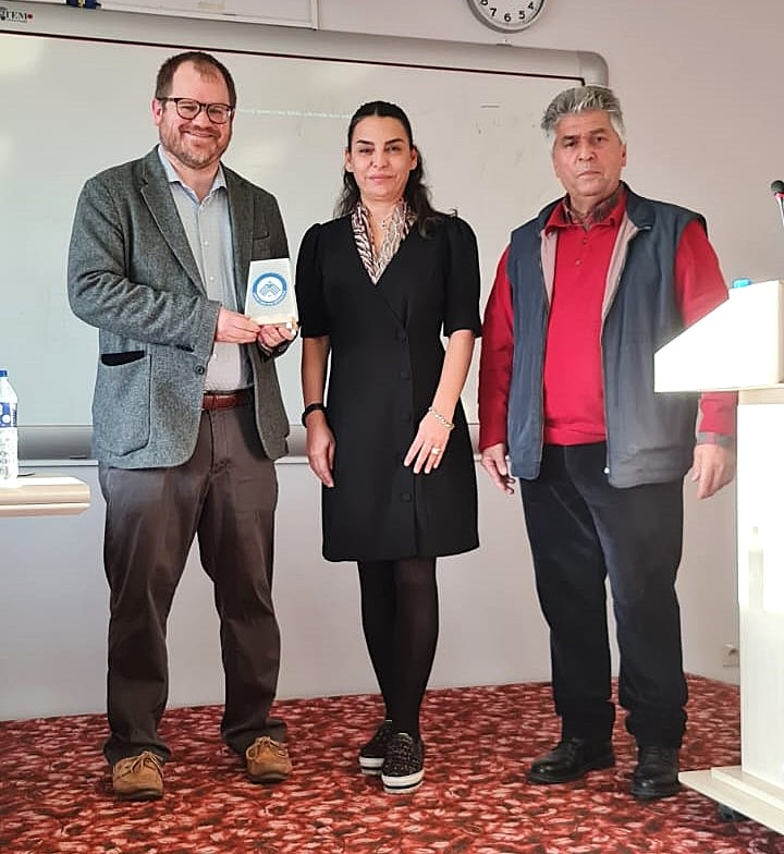 Three humanities faculty stand next to each other with one holding a blue and white plaque.