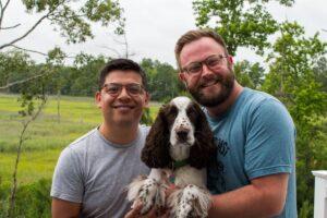 Dave Anguish and another adult stand side by side holding a black and white puppy between them