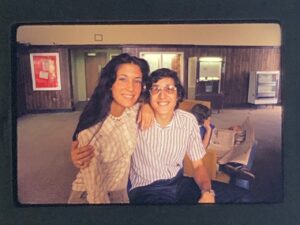 A photo from the 70s of a young man and woman smiling and sitting together in a room with wood-paneling and vending machines.