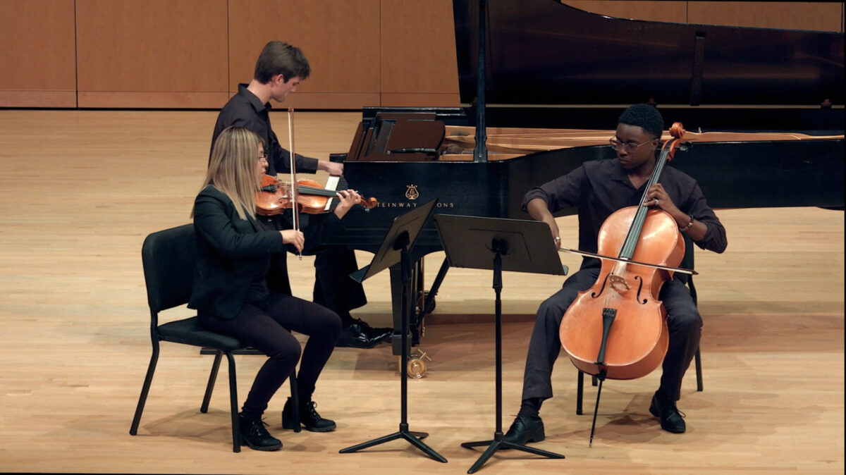 cellist, violinist, pianist dressed in all black perform on stage
