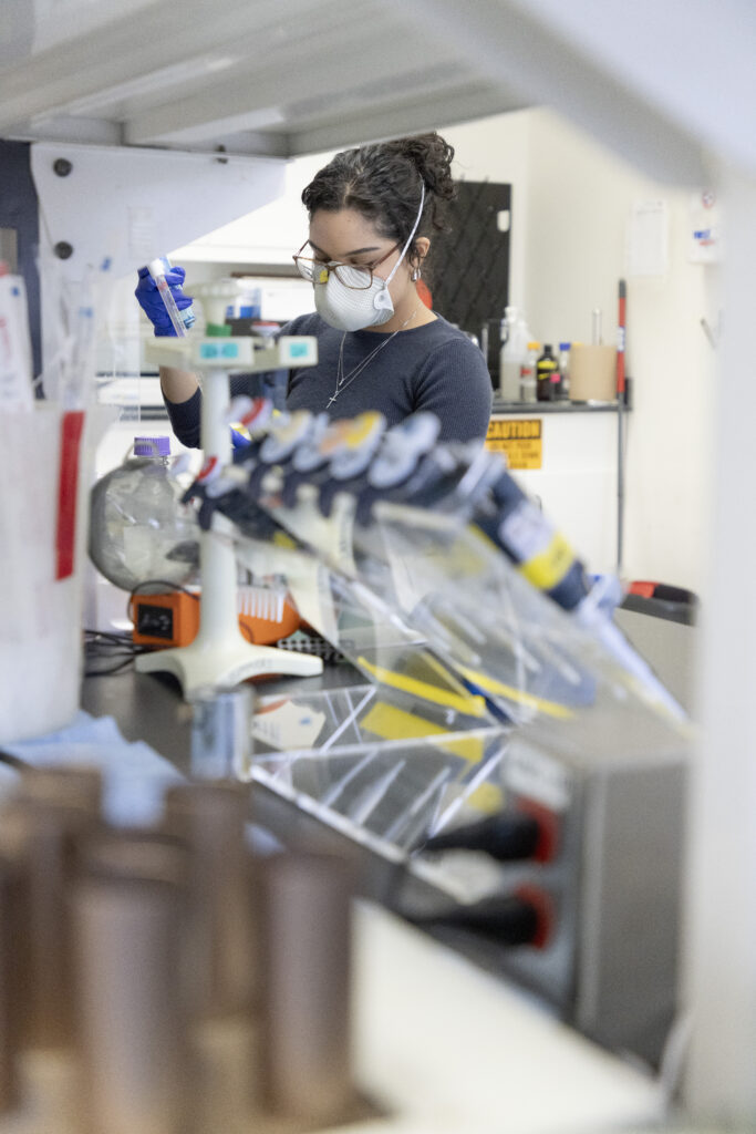 woman working with a pipet, wearing a face mask, in a laboratory