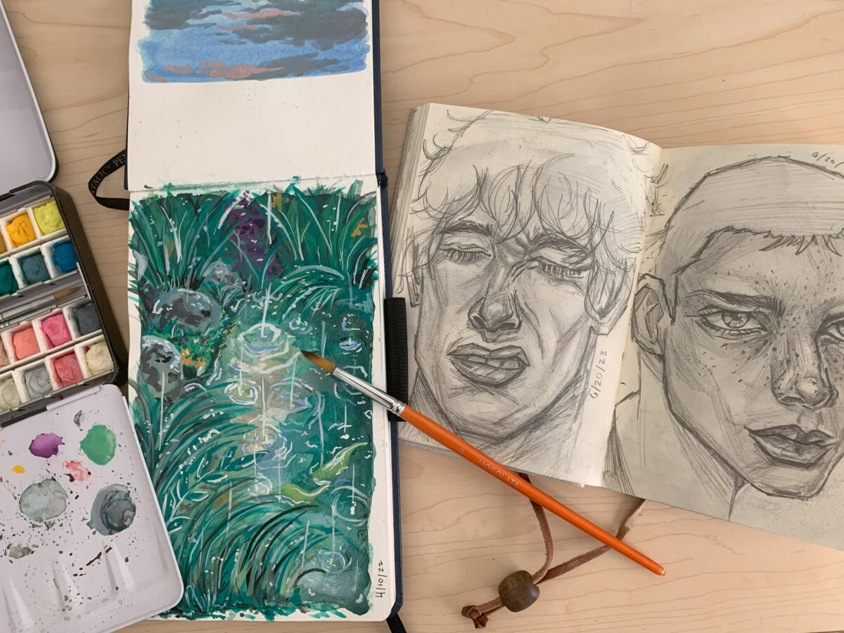 pencil sketches of faces, a pad with a painting of green grasses, and a paint palette