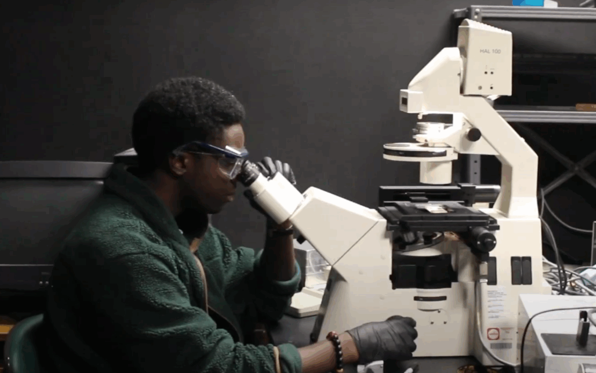 young man wearing safety glasses peers into a microscope