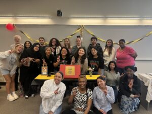 A large group of students holding up peace signs stand around a social work info table