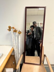 Two people taking a selfie in a mirror, surrounded by room furnishings and decorations.