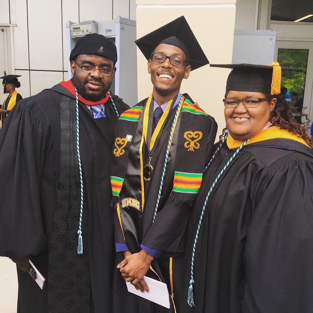 Three people stand in graduation regalia