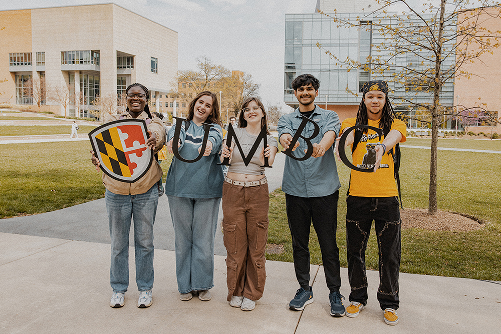 a diverse group of students holding up the UMBC maryland shield and letters