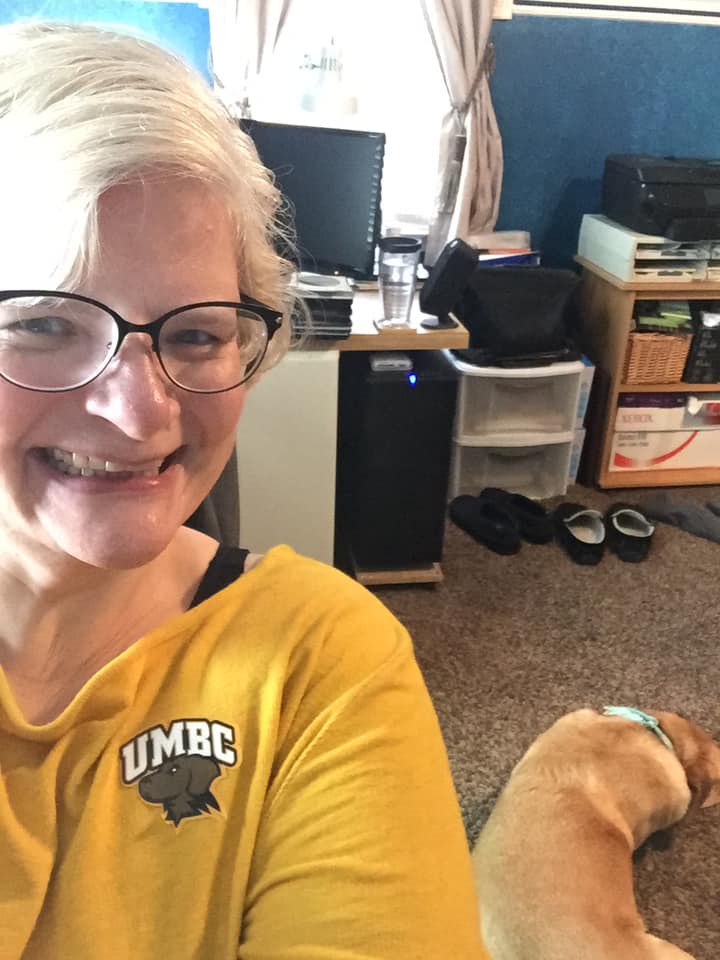 a woman in a gold shirt smiling with a dog sleeping on the floor next to her