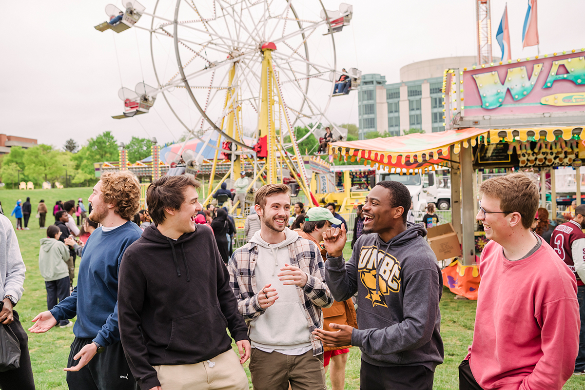 a group of students at umbc's quadmania carnival with a ferris wheel behind them