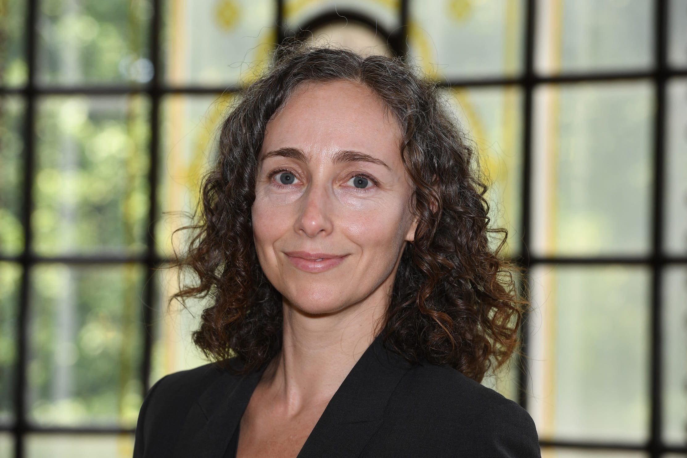 A white woman with dark curly hair and a dark top smiles at the camera.