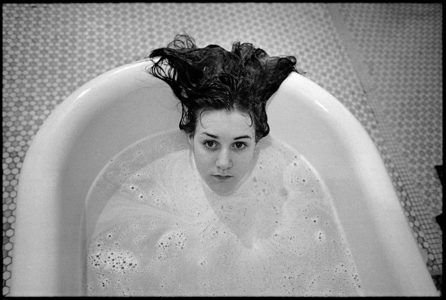 In a black and white photo, a woman with dark hair is submerged in a bathtub, with only her head visible.