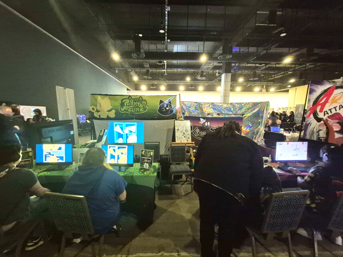 People sit at computers and play games. Nearby booths display game names.