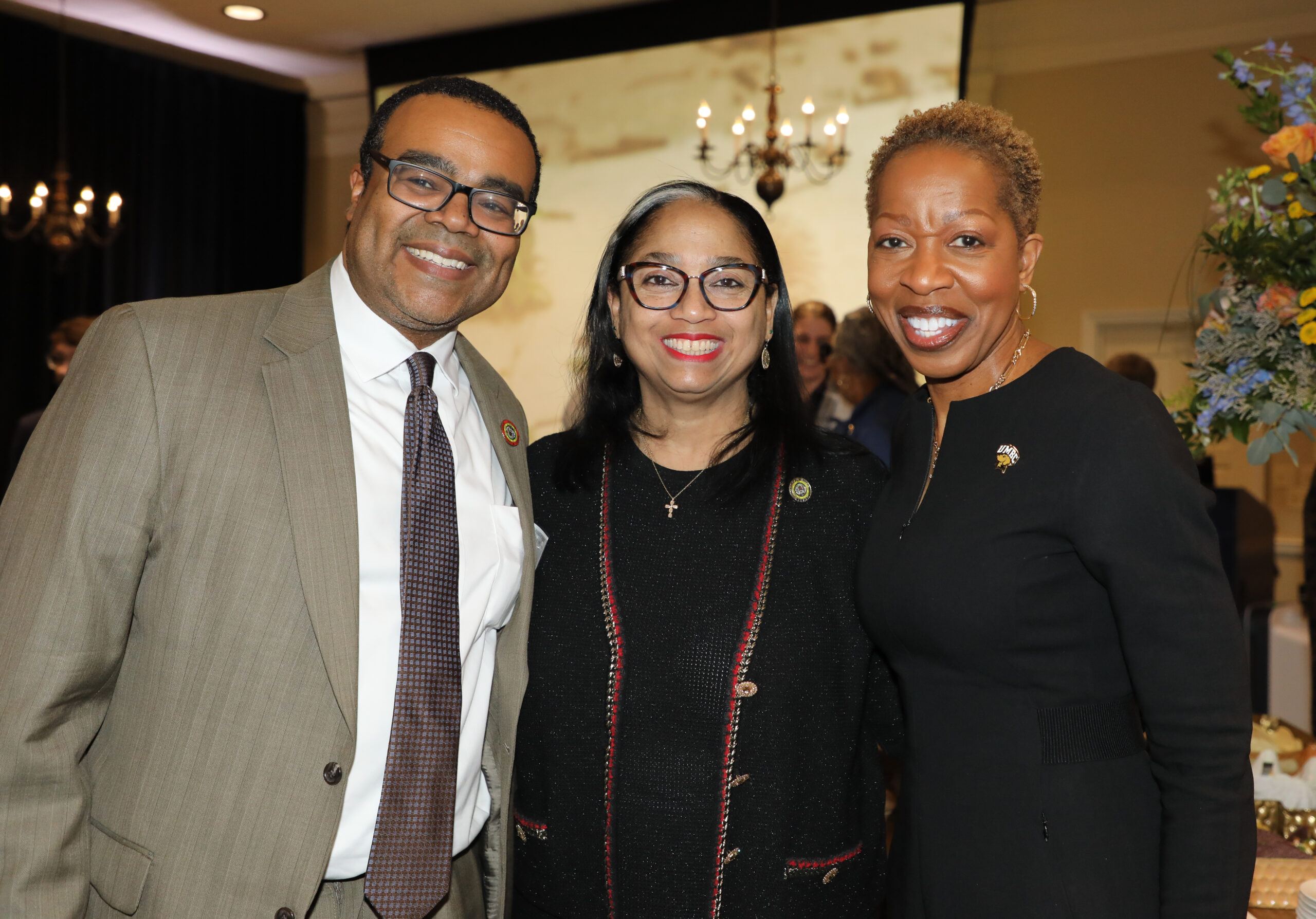 Three leaders, a man and two women in business attire, pose at an event.