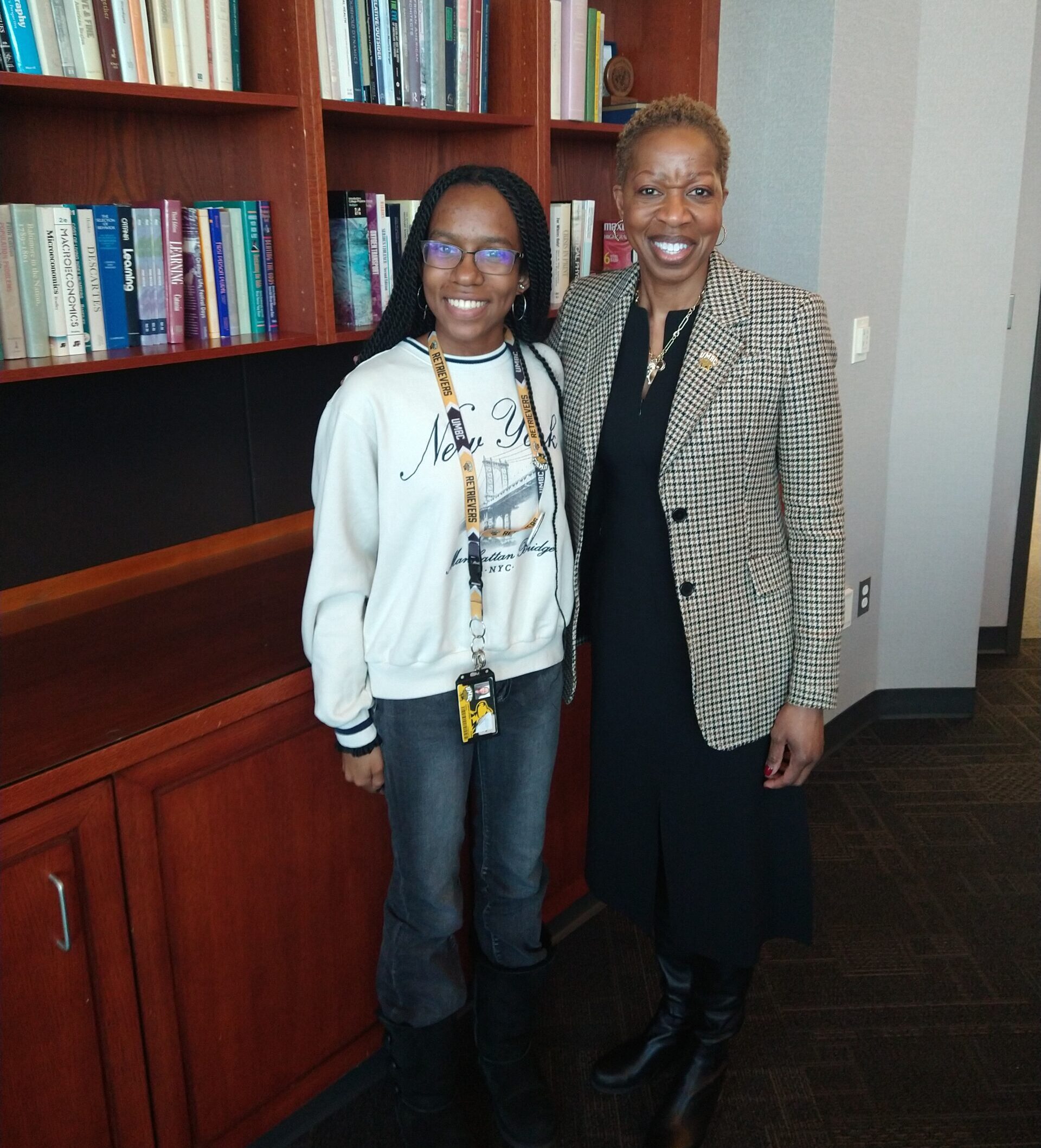 A student with a Retriever lanyard around her neck stands with President Sheares Ashby in front of a bookcase.