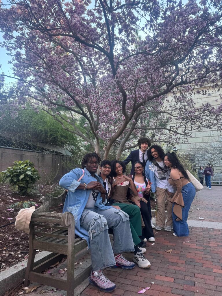 group of smiling students on a bench in a park, blooming magnolia tree in background