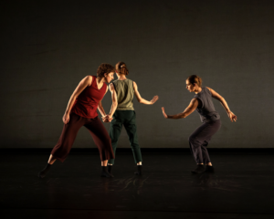 Against a dimmed background, three dancers perform on stage.