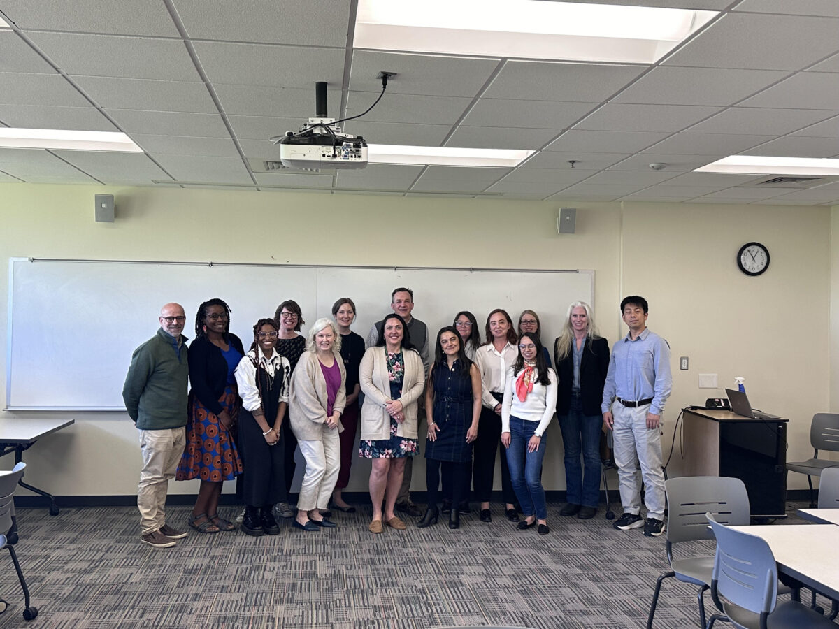 Fifteen university faculty and staff gather at the front of a classroom for a group picture UMBC Global Learning Lab