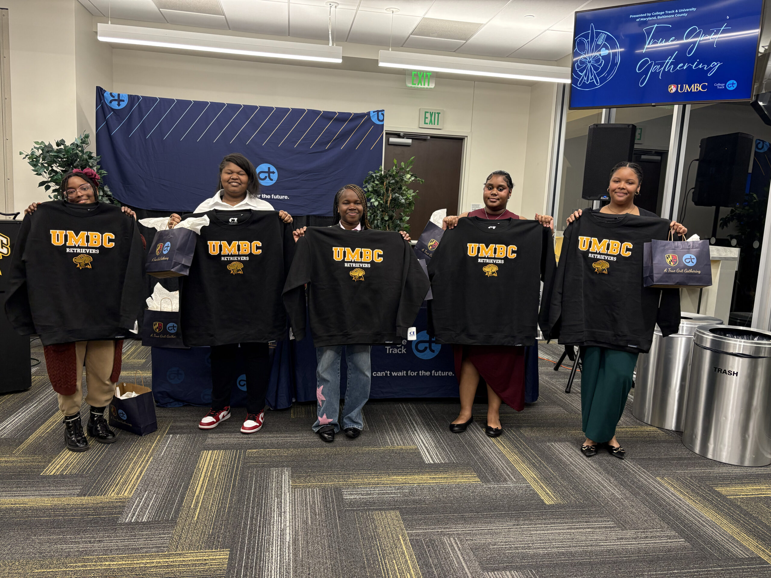 Students stand in a line holding up UMBC sweatshirts