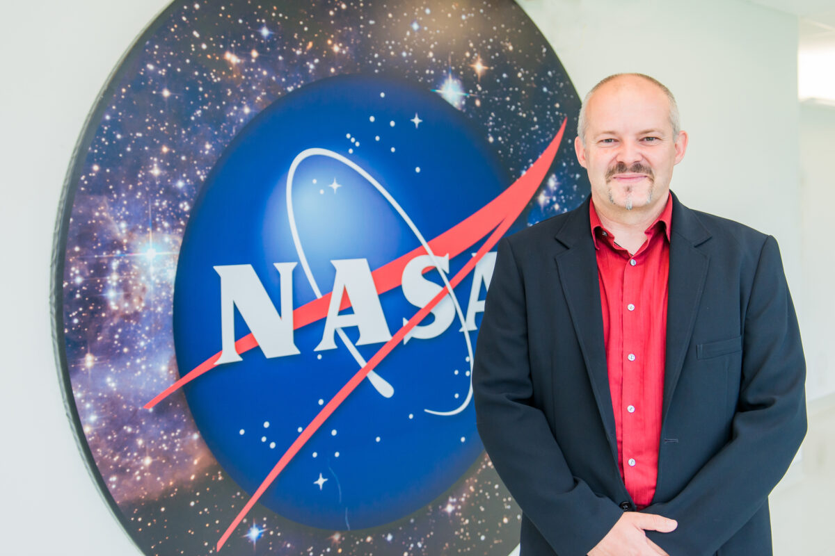 portrait of Jan Merka, previous leader of the Goddard Planetary Heliophysics Institute, in front of large NASA logo