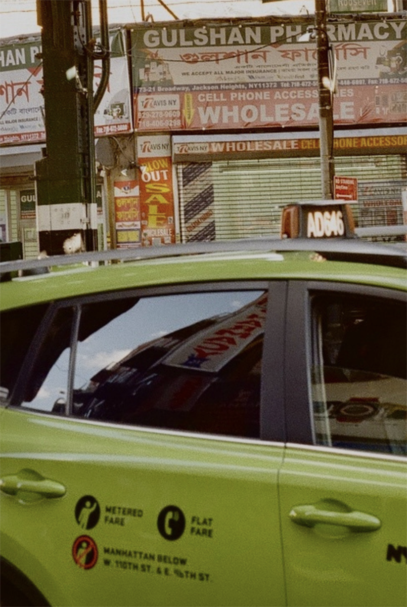 In the foreground, the side of a green taxi, and in the background a complex storefront that says Gulshan Pharmacy and Wholesale. Image by Vaniya Khan.