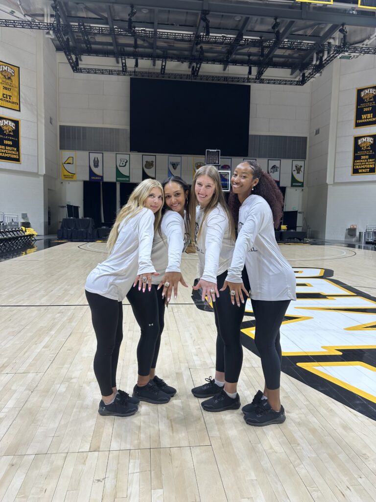 Four women pose, showing off their team rings