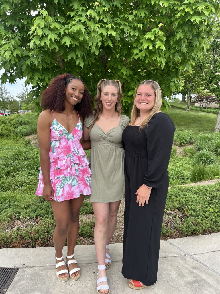 Three women stand together smiling for the camera